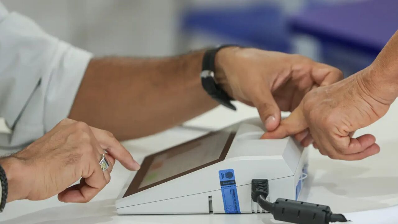 Mesário confere a digital de uma eleitora no leitor biométrico da urna eletrônica