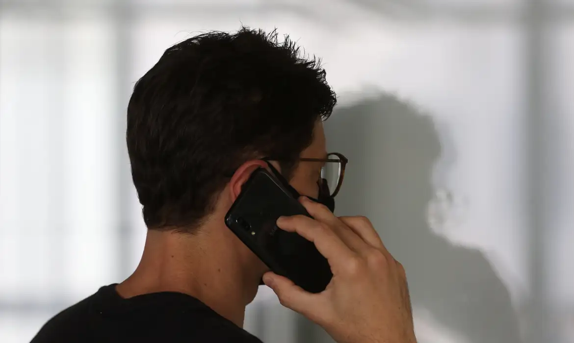 Pessoa segurando um telefone celular em uso. Foto: Tânia Rêgo/Agência Brasil