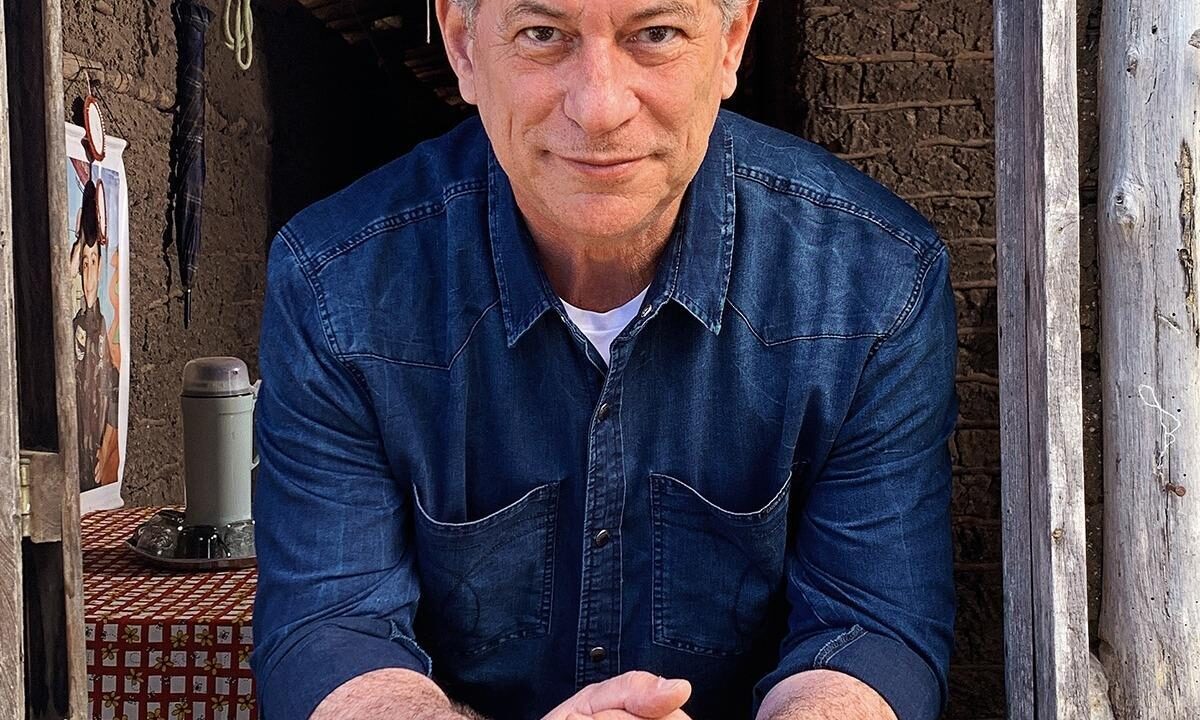 Ciro Gomes debruçado em uma janela de madeira de uma casa de taipa
