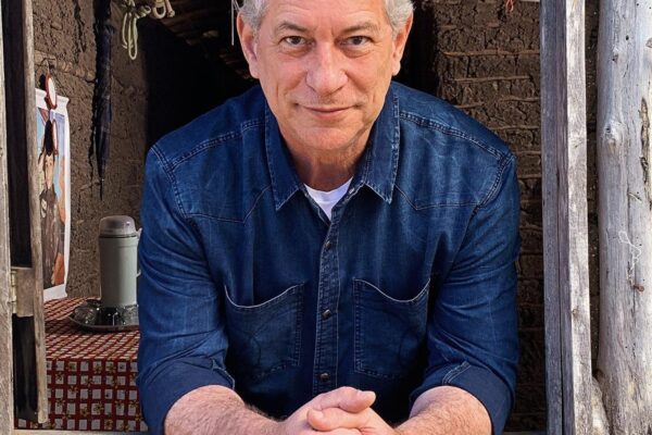 Ciro Gomes debruçado em uma janela de madeira de uma casa de taipa